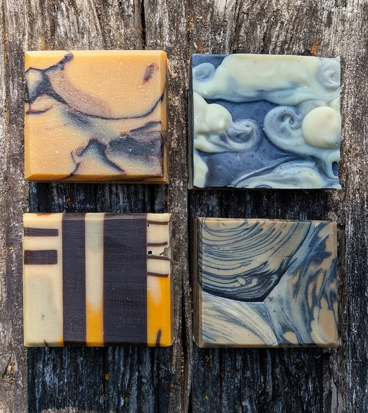 Four goat milk soaps representing the four seasons Earth, Air, Fire, Water lay face up on a wood background